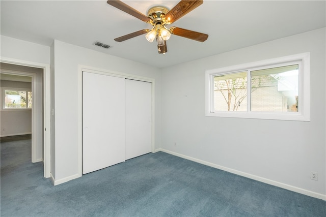 unfurnished bedroom featuring a closet, multiple windows, dark colored carpet, and ceiling fan