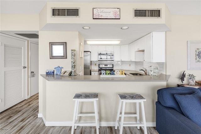 kitchen featuring appliances with stainless steel finishes, white cabinetry, sink, kitchen peninsula, and a breakfast bar area