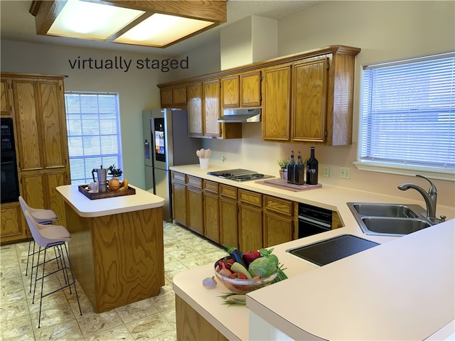 kitchen featuring brown cabinetry, a kitchen breakfast bar, under cabinet range hood, black appliances, and a sink