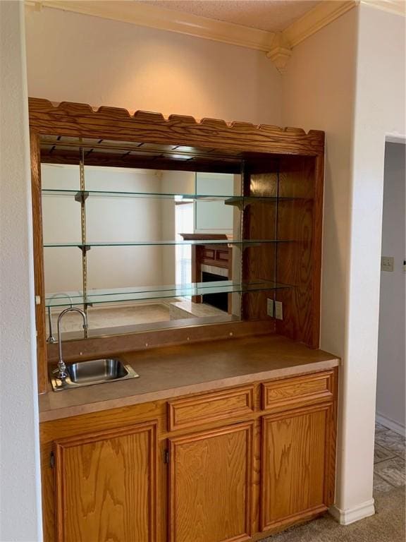 bar featuring light colored carpet, a fireplace, a sink, baseboards, and crown molding