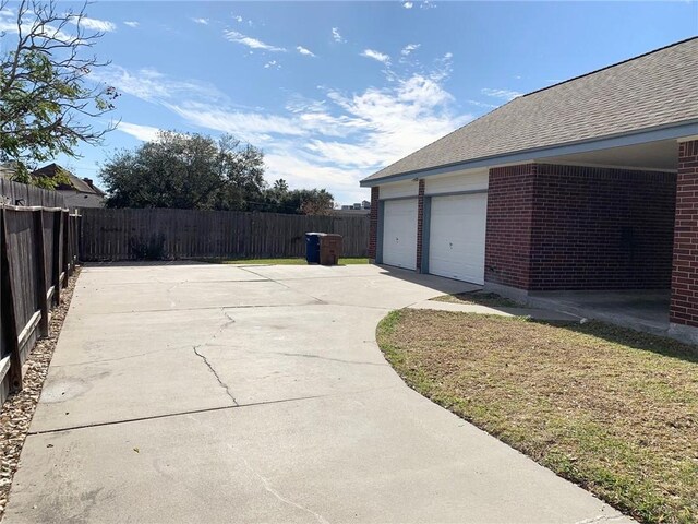 exterior space featuring a shingled roof, brick siding, fence, and an attached garage