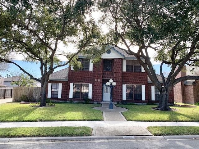 view of front of home with roof with shingles, a front yard, fence, and brick siding