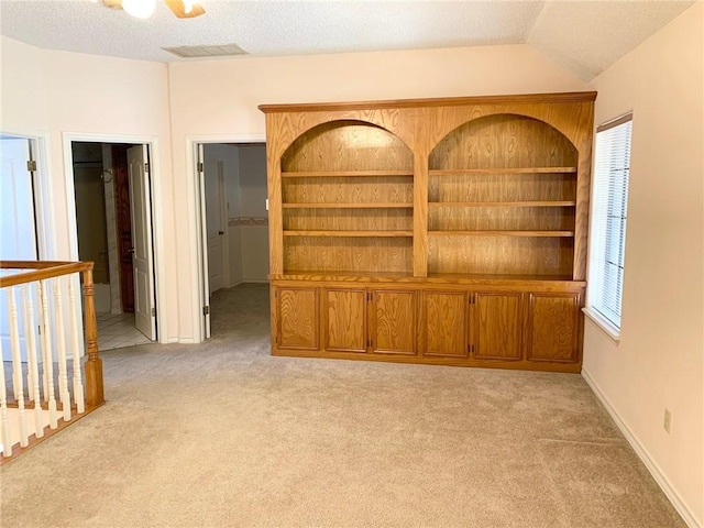 carpeted empty room with built in shelves, a textured ceiling, and lofted ceiling