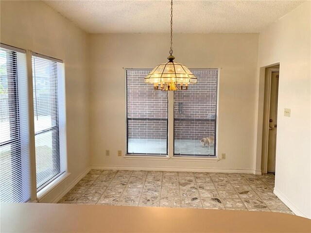 unfurnished dining area featuring a textured ceiling, a chandelier, and baseboards