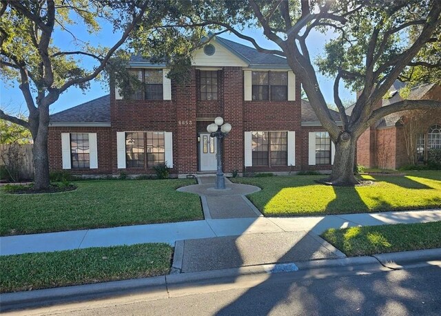 view of front of property featuring a front yard, brick siding, and roof with shingles