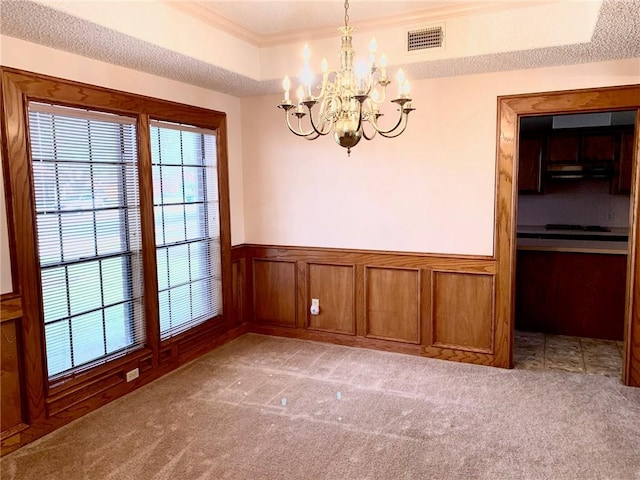 unfurnished dining area with visible vents, a raised ceiling, a wainscoted wall, ornamental molding, and carpet floors