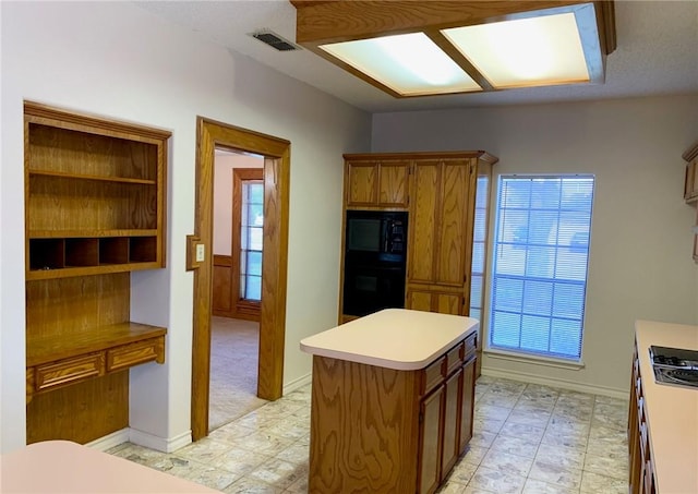 kitchen featuring a center island, brown cabinets, light countertops, visible vents, and black appliances