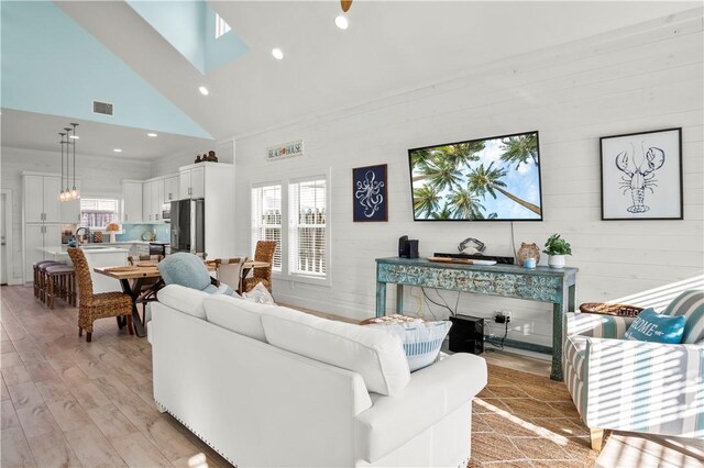 living room with a healthy amount of sunlight, high vaulted ceiling, and light hardwood / wood-style floors