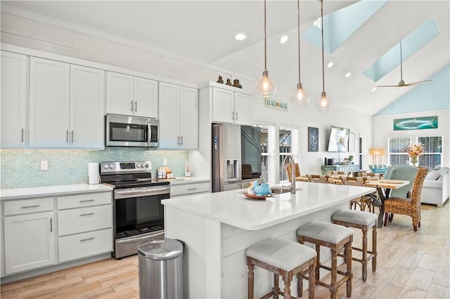 kitchen with appliances with stainless steel finishes, a kitchen island with sink, a skylight, white cabinets, and decorative light fixtures