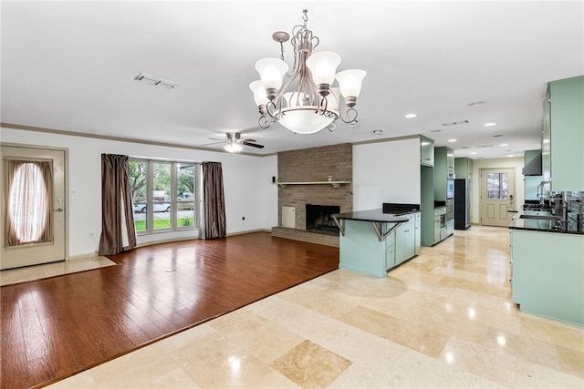 kitchen with a brick fireplace, ceiling fan with notable chandelier, decorative light fixtures, a breakfast bar area, and green cabinets