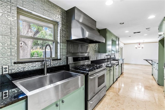 kitchen featuring sink, stainless steel gas range oven, green cabinets, and wall chimney range hood