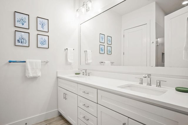 bathroom featuring double vanity, baseboards, a sink, and wood finished floors