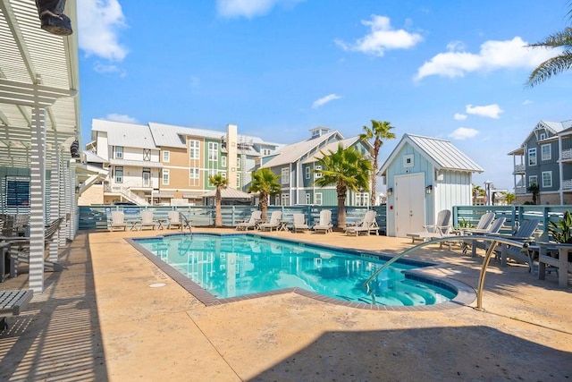 community pool with a residential view, a patio, a storage shed, and fence