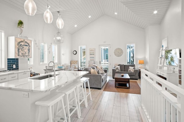 kitchen with light wood finished floors, light stone counters, a kitchen bar, white cabinetry, and a sink