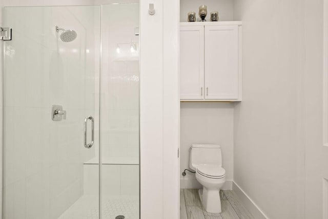 bathroom with toilet, a stall shower, and baseboards