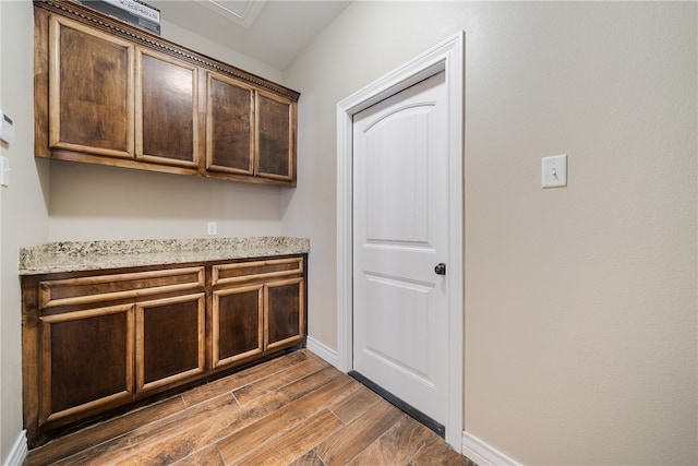 kitchen featuring dark wood-type flooring, dark brown cabinetry, and light stone counters