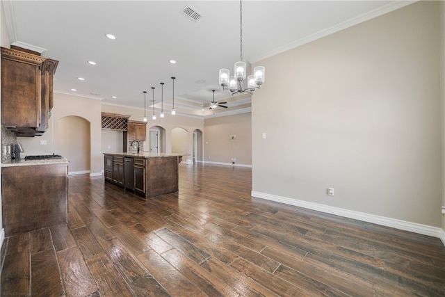 kitchen featuring ornamental molding, ceiling fan with notable chandelier, an island with sink, pendant lighting, and dark hardwood / wood-style flooring