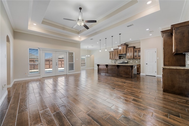 unfurnished living room with dark wood-type flooring, ceiling fan, crown molding, and a tray ceiling