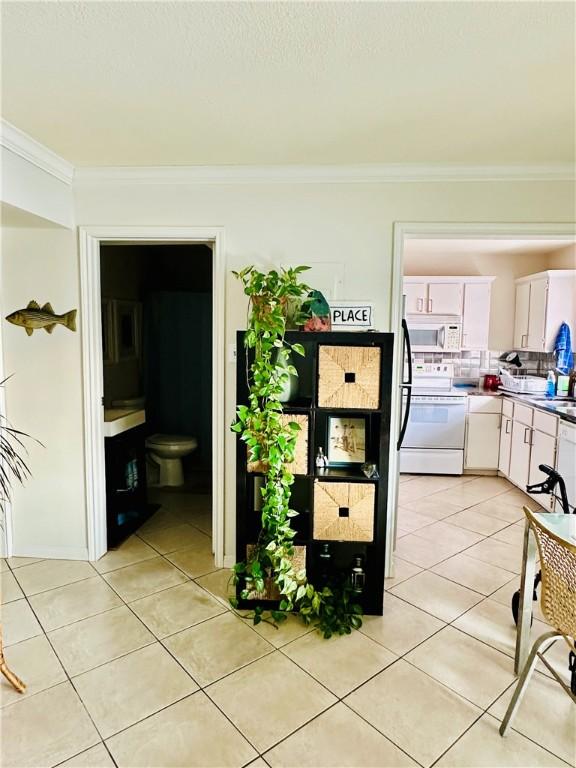 interior space with light tile patterned floors, ornamental molding, white cabinets, and white appliances