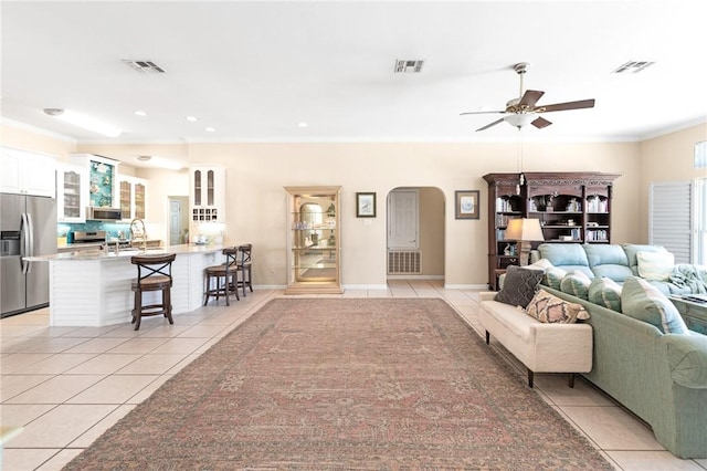 living area featuring light tile patterned flooring, arched walkways, ceiling fan, ornamental molding, and recessed lighting