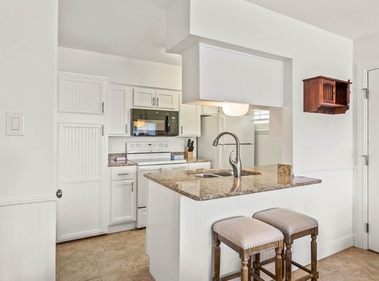 kitchen with a breakfast bar, kitchen peninsula, white appliances, stone counters, and white cabinets