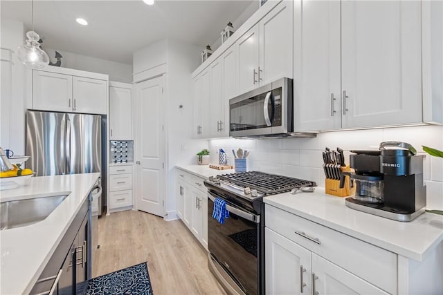 kitchen with light wood-style flooring, light countertops, appliances with stainless steel finishes, white cabinetry, and tasteful backsplash