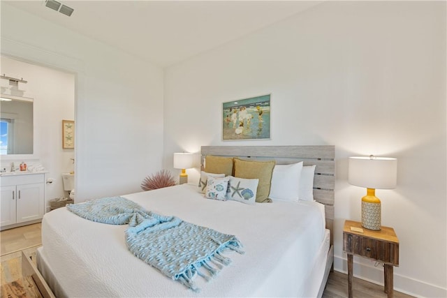 bedroom featuring baseboards, visible vents, a sink, light wood-type flooring, and connected bathroom