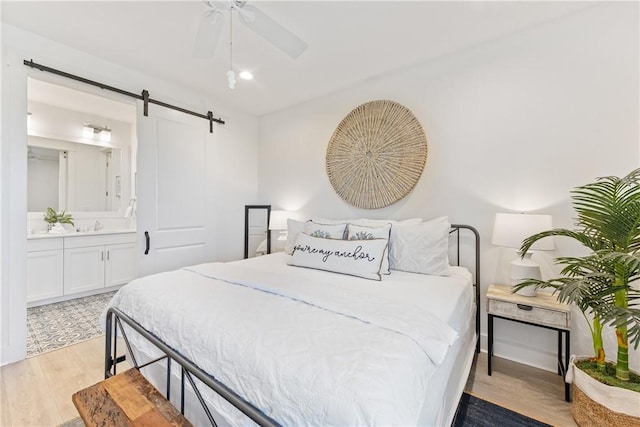 bedroom with recessed lighting, ceiling fan, light wood-style floors, a barn door, and connected bathroom