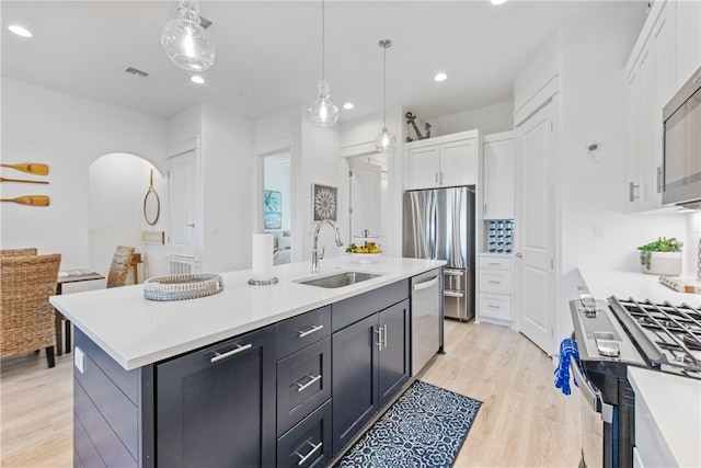 kitchen featuring a sink, appliances with stainless steel finishes, arched walkways, white cabinetry, and a kitchen island with sink