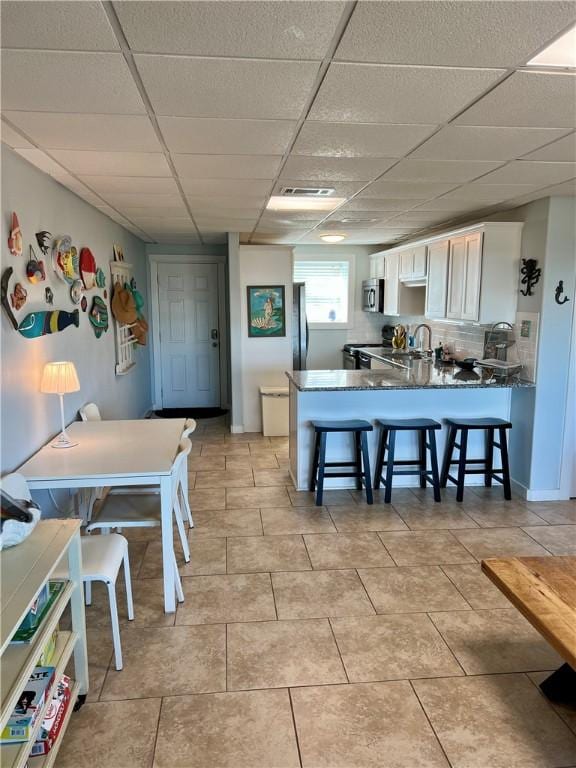 kitchen with a paneled ceiling, white cabinetry, decorative backsplash, kitchen peninsula, and a breakfast bar