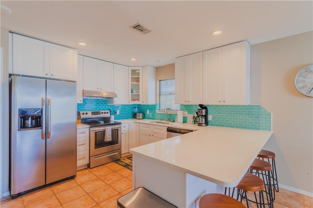 122 Palm Dr, Rockport, TX 78382 - kitchen featuring under cabinet range hood, stainless steel appliances, a peninsula, a breakfast bar area, and light countertops