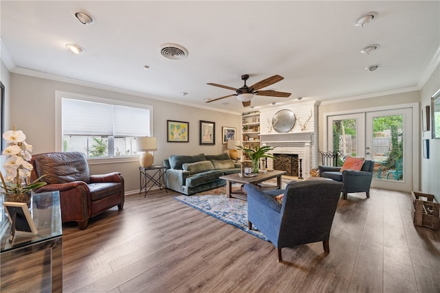 living room with a wealth of natural light, hardwood / wood-style floors, ornamental molding, and a fireplace