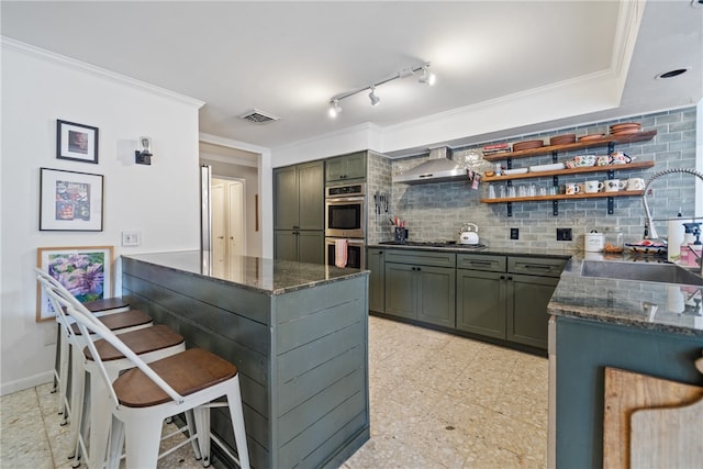 kitchen featuring stainless steel appliances, wall chimney exhaust hood, sink, tasteful backsplash, and ornamental molding