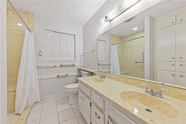 bathroom featuring tile patterned floors, toilet, a tile shower, double vanity, and baseboards