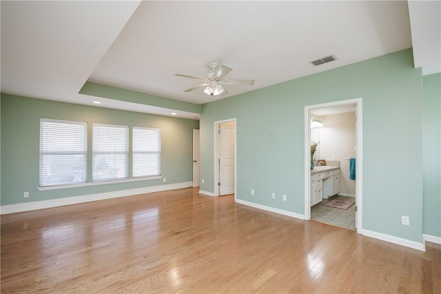 unfurnished bedroom with connected bathroom, visible vents, baseboards, light wood finished floors, and a walk in closet