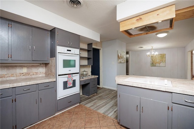 kitchen featuring visible vents, double oven, gray cabinets, and tile counters