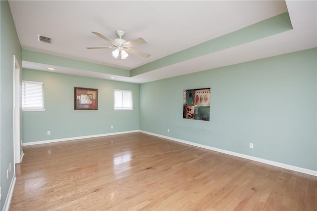 spare room with light wood finished floors, visible vents, baseboards, ceiling fan, and a tray ceiling