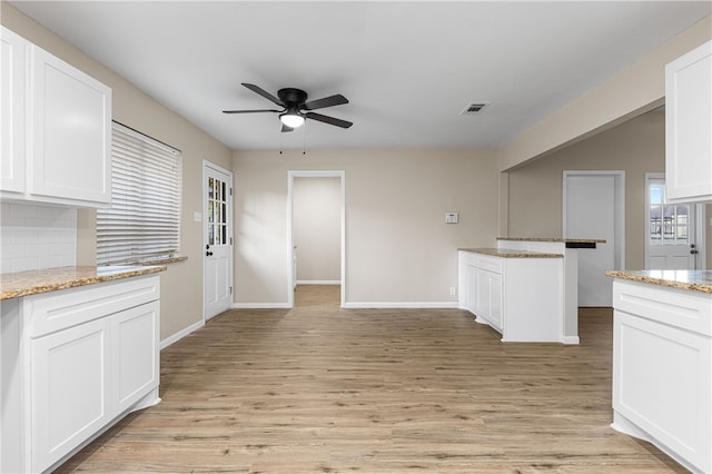 kitchen with white cabinetry, light wood-type flooring, and light stone countertops