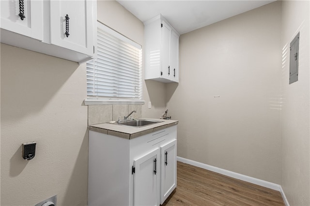 laundry area with cabinets, sink, light hardwood / wood-style flooring, and electric panel