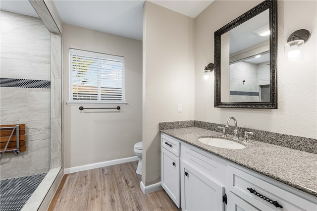 bathroom with hardwood / wood-style floors, vanity, toilet, and tiled shower