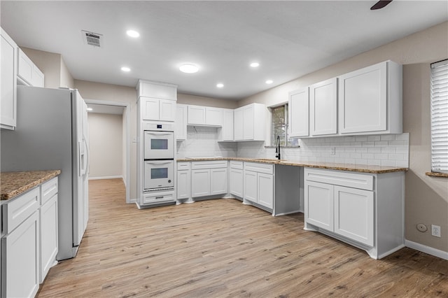 kitchen with white cabinetry, light stone countertops, white appliances, light wood-type flooring, and decorative backsplash