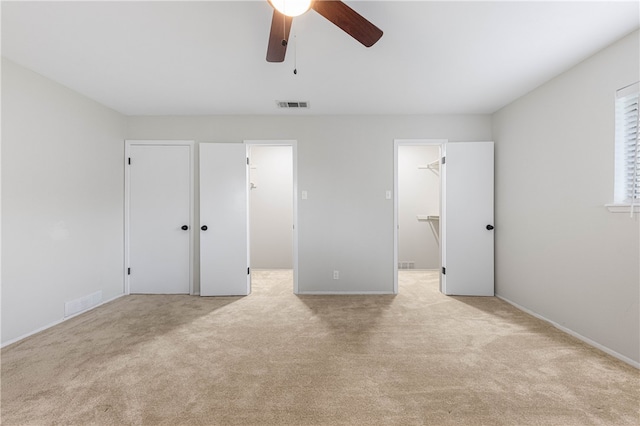 unfurnished bedroom with light colored carpet, ceiling fan, a walk in closet, and a closet