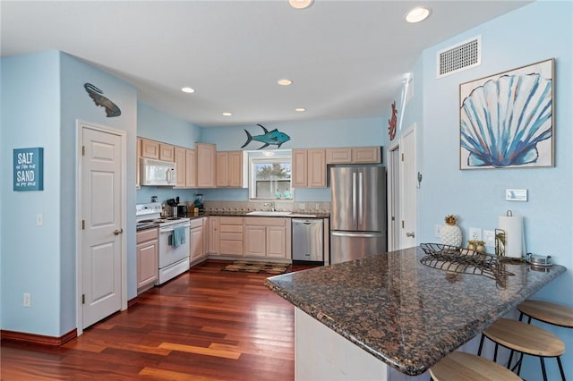 kitchen with appliances with stainless steel finishes, a peninsula, dark wood-style floors, a sink, and a breakfast bar area