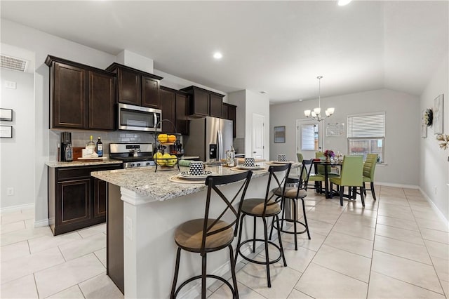 kitchen featuring light tile patterned floors, a breakfast bar area, a kitchen island with sink, stainless steel appliances, and tasteful backsplash