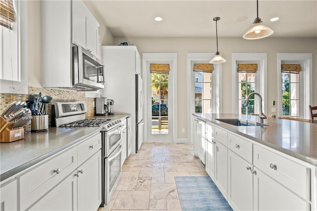 kitchen featuring backsplash, white cabinets, sink, appliances with stainless steel finishes, and decorative light fixtures