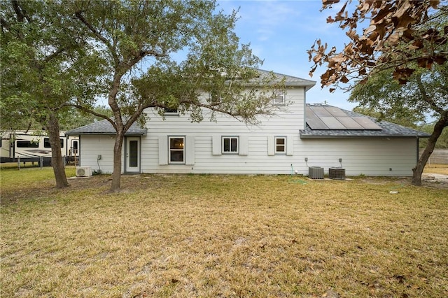 back of property with a yard, solar panels, and central air condition unit