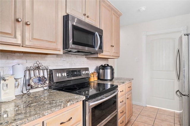 kitchen with stainless steel appliances, dark stone countertops, light tile patterned floors, and light brown cabinetry