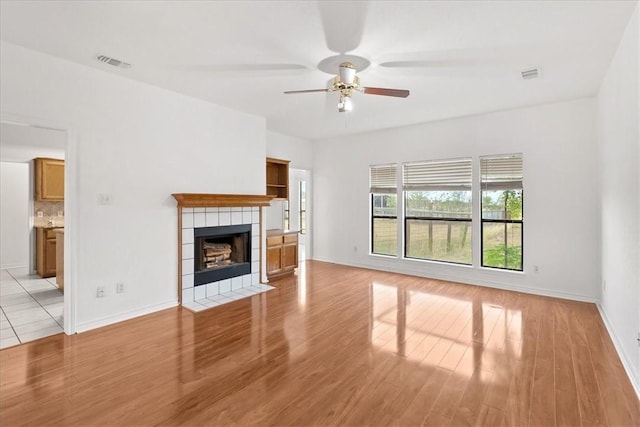 unfurnished living room with a tiled fireplace, ceiling fan, and light hardwood / wood-style flooring