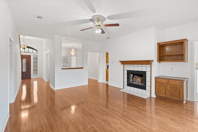 unfurnished living room featuring ceiling fan with notable chandelier, light wood-type flooring, and a fireplace