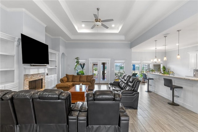 living room featuring a raised ceiling, crown molding, a stone fireplace, and light wood-type flooring